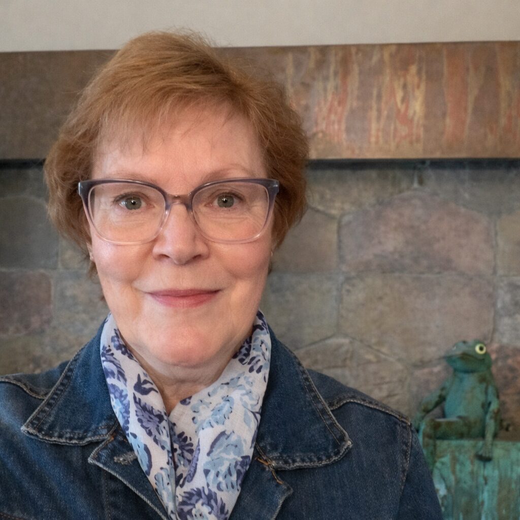 Therapist, Carolyn Feeheley with a gentle smile, standing in front of a stone wall.